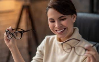 Making choice. A young woman holding two pairs of eyeglasses and smiling